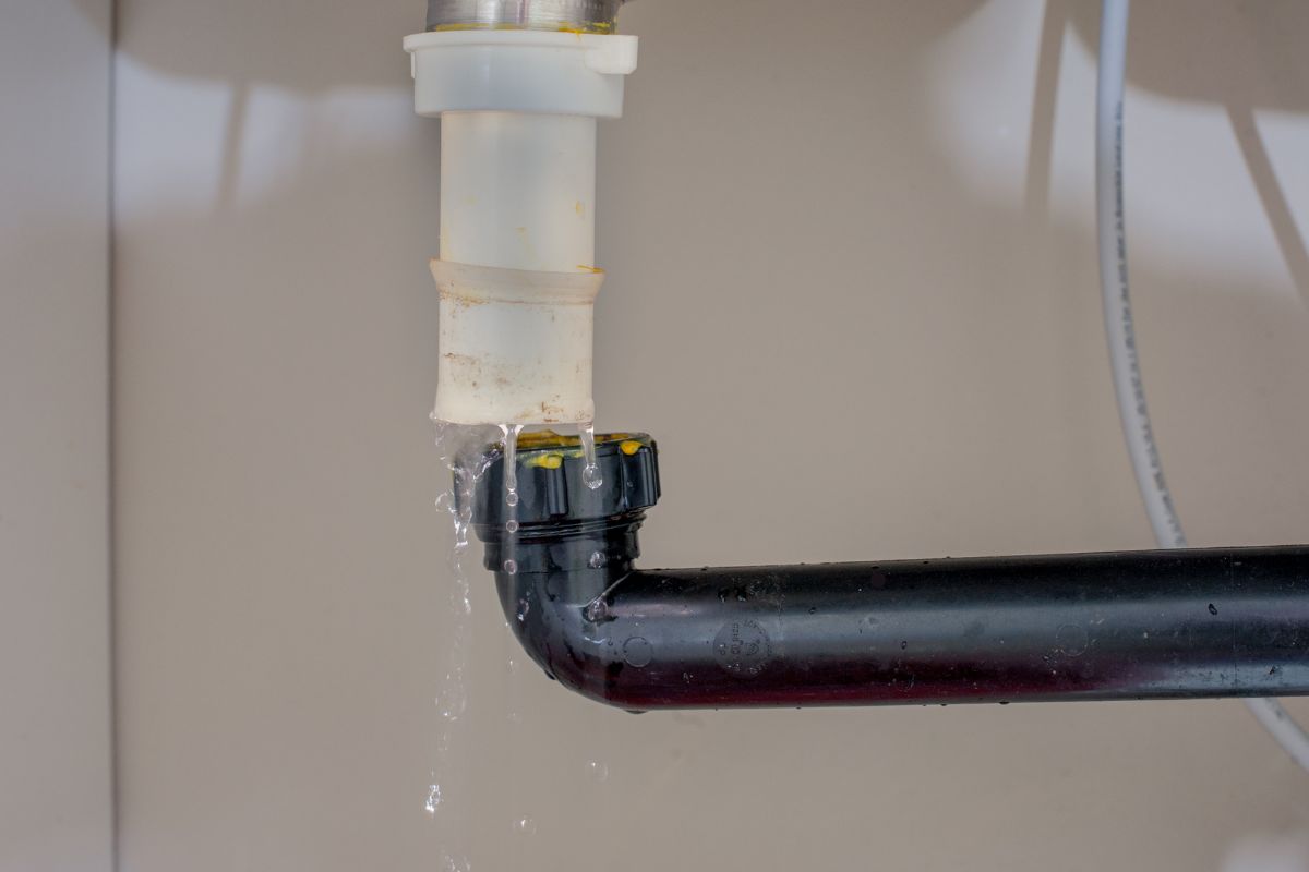 A landlord fixing a leaky pipe, with water flowing out, during routine property maintenance.